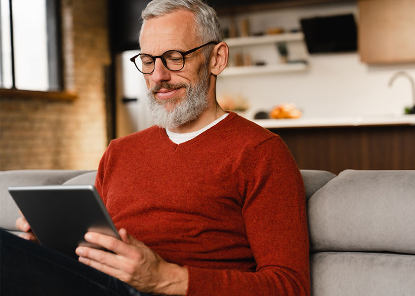 Man in red sweater sitting on couch looking at tablet